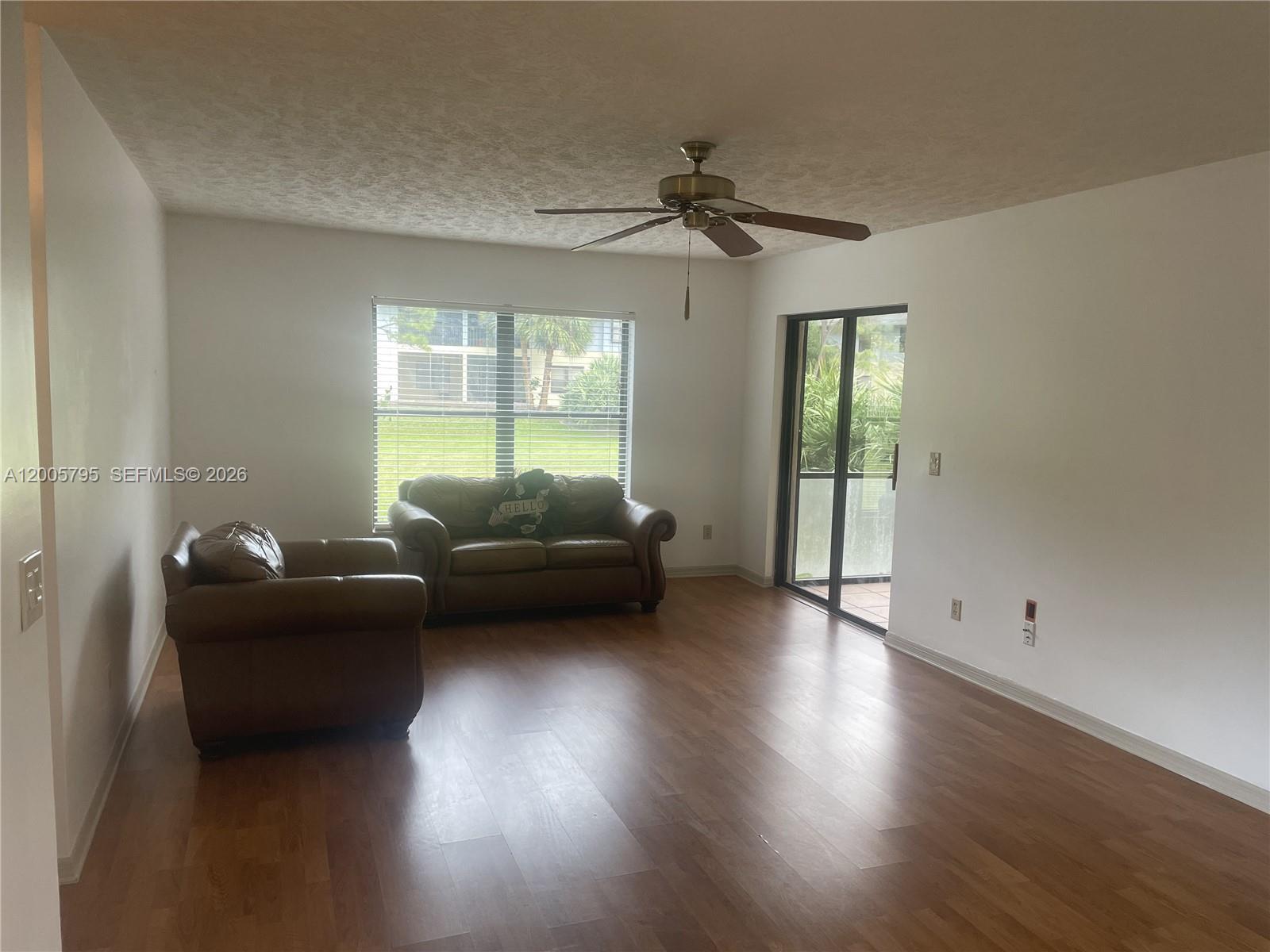 A living room features wood-look flooring, a ceiling fan, a window, and sliding glass doors — 6553 SE Federal Hwy # 102, Stuart FL 34997, STUART, FL