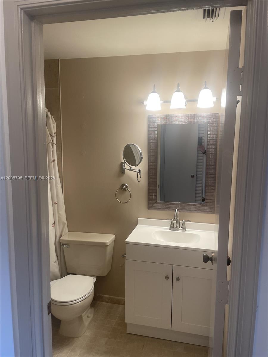 A small bathroom features a white vanity, a framed mirror, and a toilet next to a shower — 6553 SE Federal Hwy # 102, Stuart FL 34997, STUART, FL