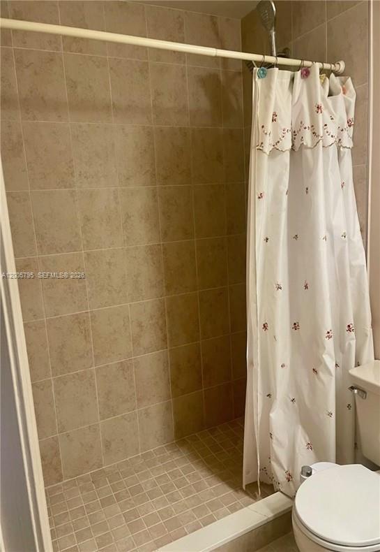 A shower stall with beige tiled walls and floor, featuring a white floral shower curtain — 6553 SE Federal Hwy # 102, Stuart FL 34997, STUART, FL