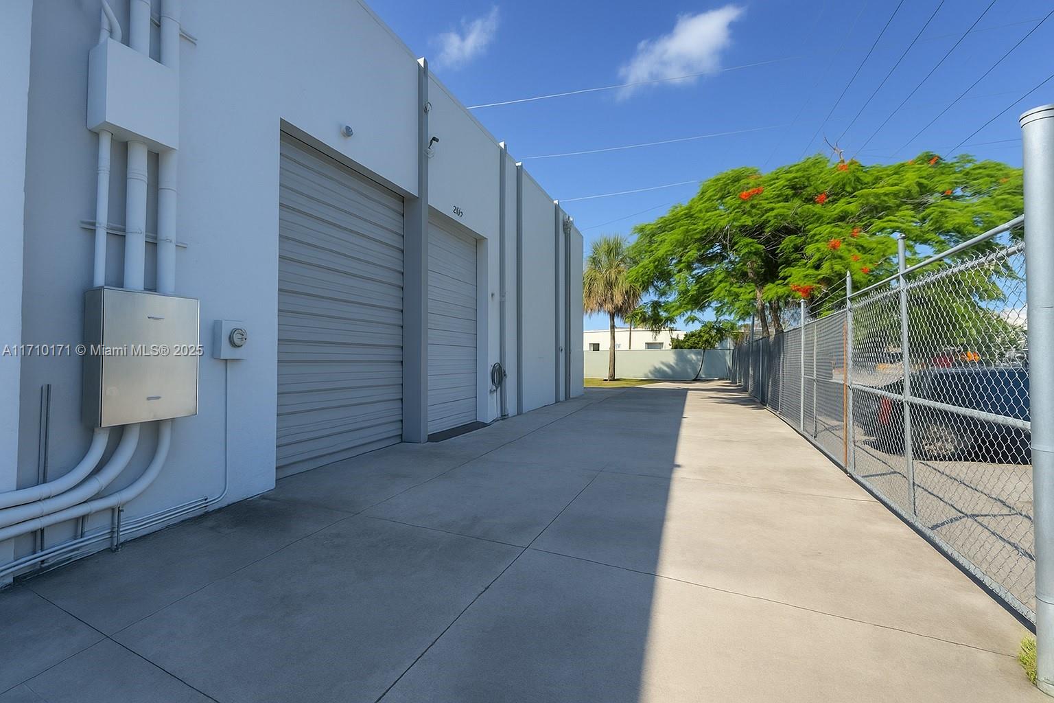 A concrete driveway runs alongside a white warehouse building with two roll-up doors and fencing — 4201 NW 37th Ct # 3728, Hialeah FL 33142, HIALEAH, FL