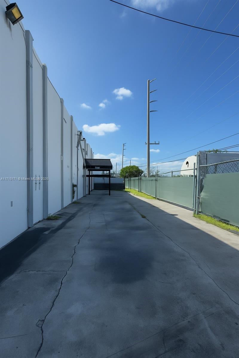 A paved exterior alleyway runs between a white building wall and a chain-link fence — 4201 NW 37th Ct # 3728, Hialeah FL 33142, HIALEAH, FL