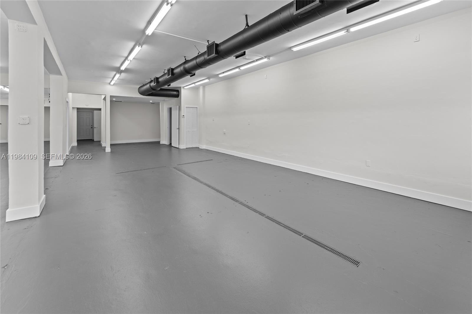 An empty commercial space features gray flooring, white walls, and exposed overhead ductwork — 5810 W Flagler St # 5810, Miami FL 33144, MIAMI, FL