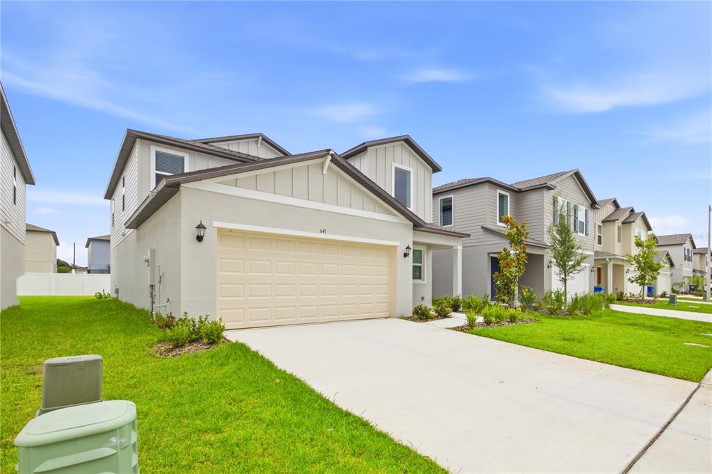 A two-story suburban house with a beige exterior, a two-car garage, and a concrete driveway — 641 BALD CYPRESS DRIVE, LAKELAND, FL