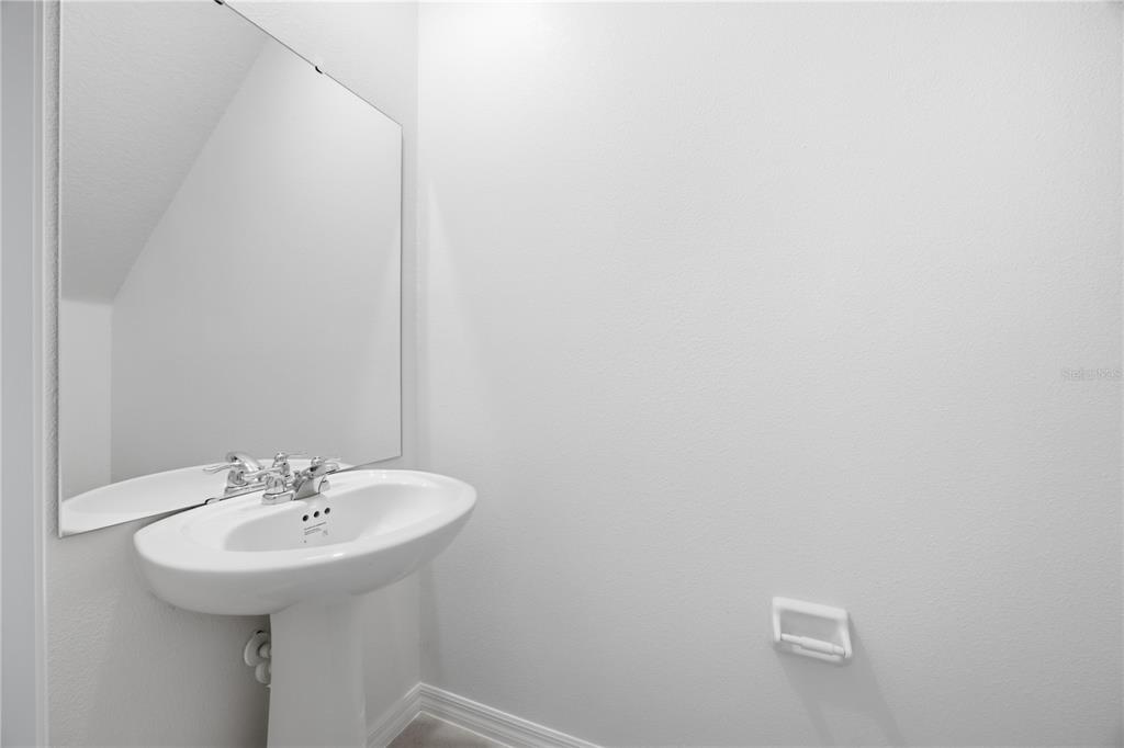 A minimalist half bathroom features a white pedestal sink, a large mirror, and light walls — 641 BALD CYPRESS DRIVE, LAKELAND, FL
