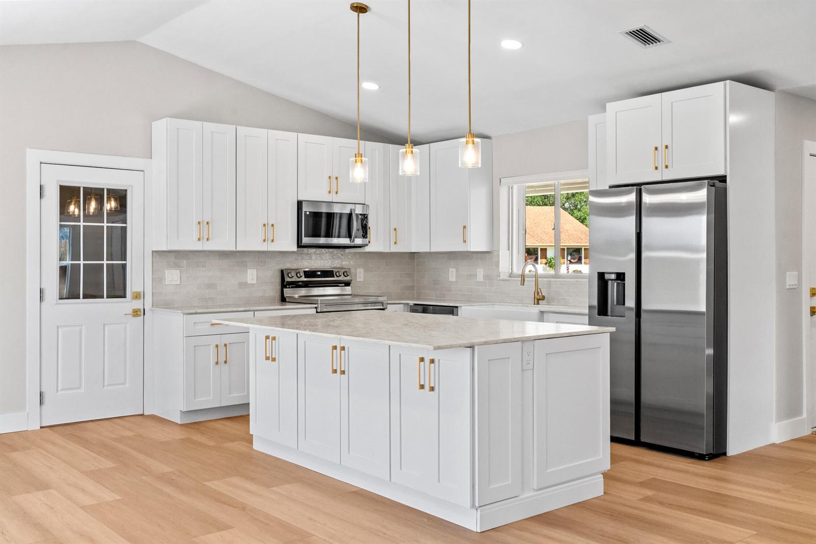 A bright kitchen features white cabinetry, a large central island, and stainless steel appliances — 74 Vista Del Rio, Boynton Beach FL 33426, BOYNTON BEACH, FL
