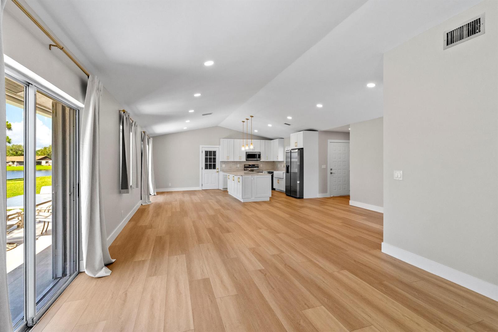 An open-concept kitchen and living area features light wood flooring, white cabinetry, and sliding doors — 74 Vista Del Rio, Boynton Beach FL 33426, BOYNTON BEACH, FL