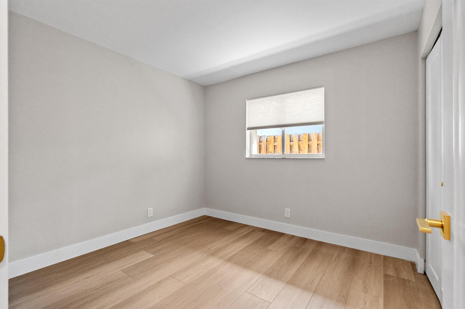An empty bedroom features light gray walls, wood-look flooring, a window with a shade, and white trim — 74 Vista Del Rio, Boynton Beach FL 33426, BOYNTON BEACH, FL