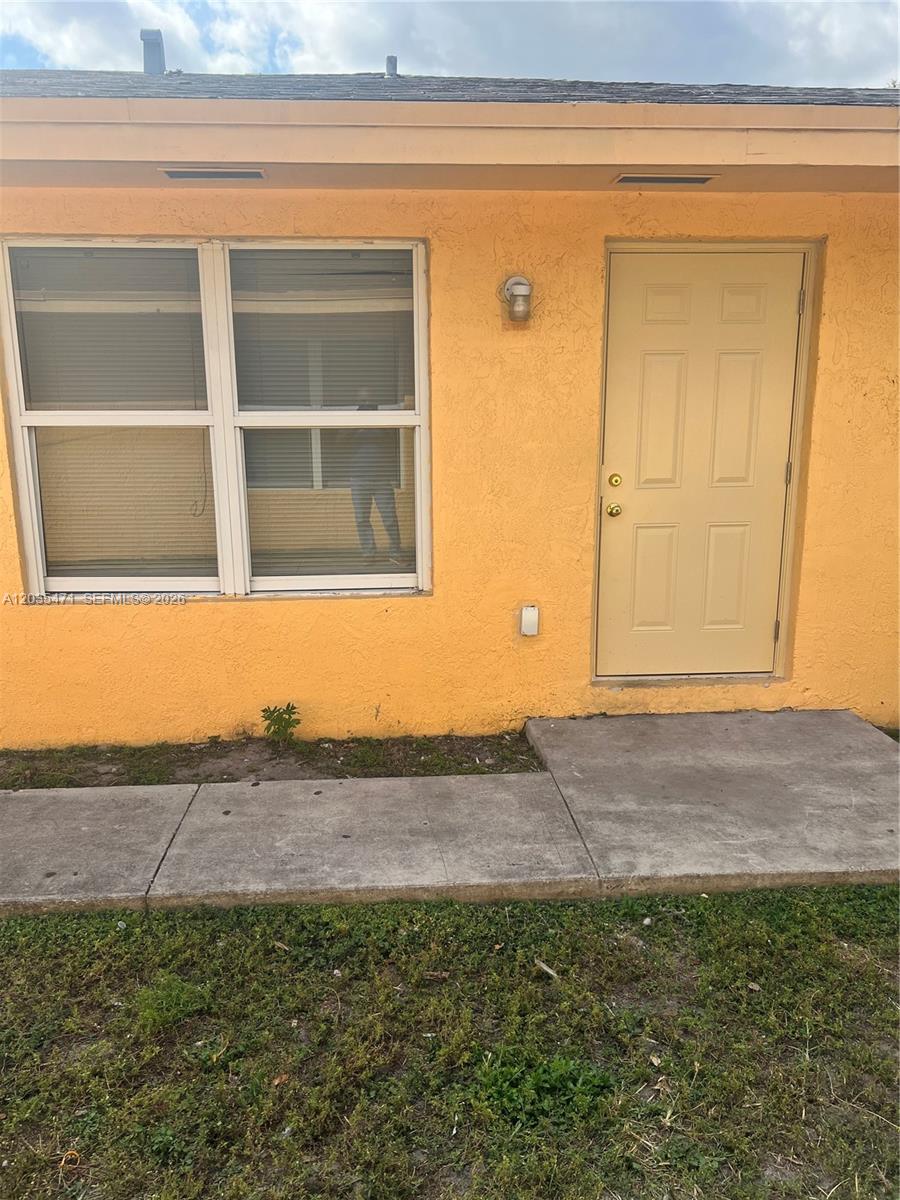 The exterior of a yellow stucco building features a window and a tan door — 2111 NW 100th St # B, Miami FL 33147, MIAMI, FL