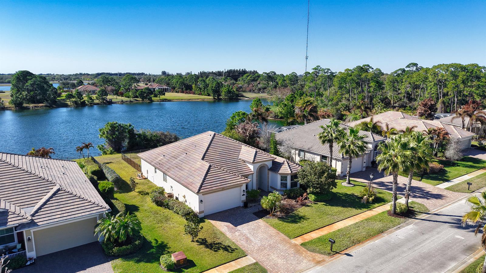 An aerial view shows suburban houses with tiled roofs situated along a lake — 7621 Fieldstone Ranch Square, Vero Beach FL 32967, VERO BEACH, FL