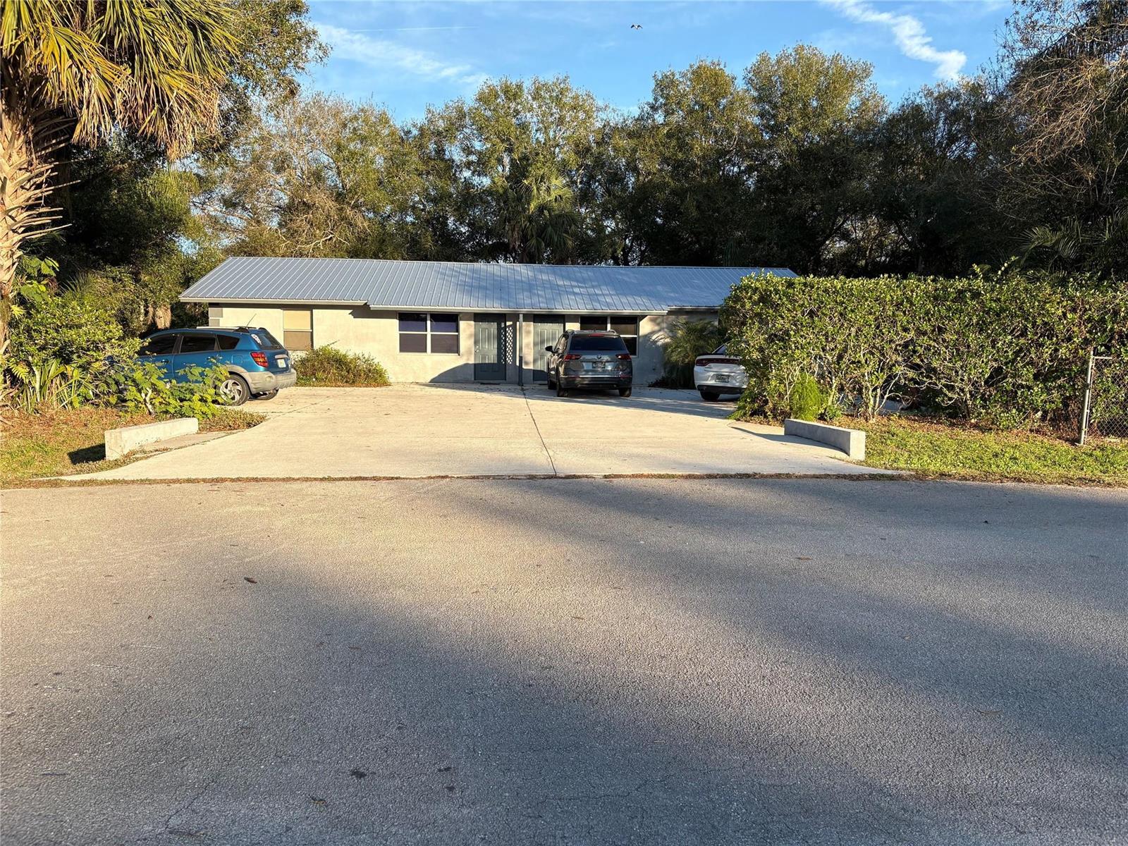 A single-story duplex with a metal roof sits behind a concrete driveway and mature trees — 540 NW 24th Avenue, Okeechobee FL 34972, OKEECHOBEE, FL