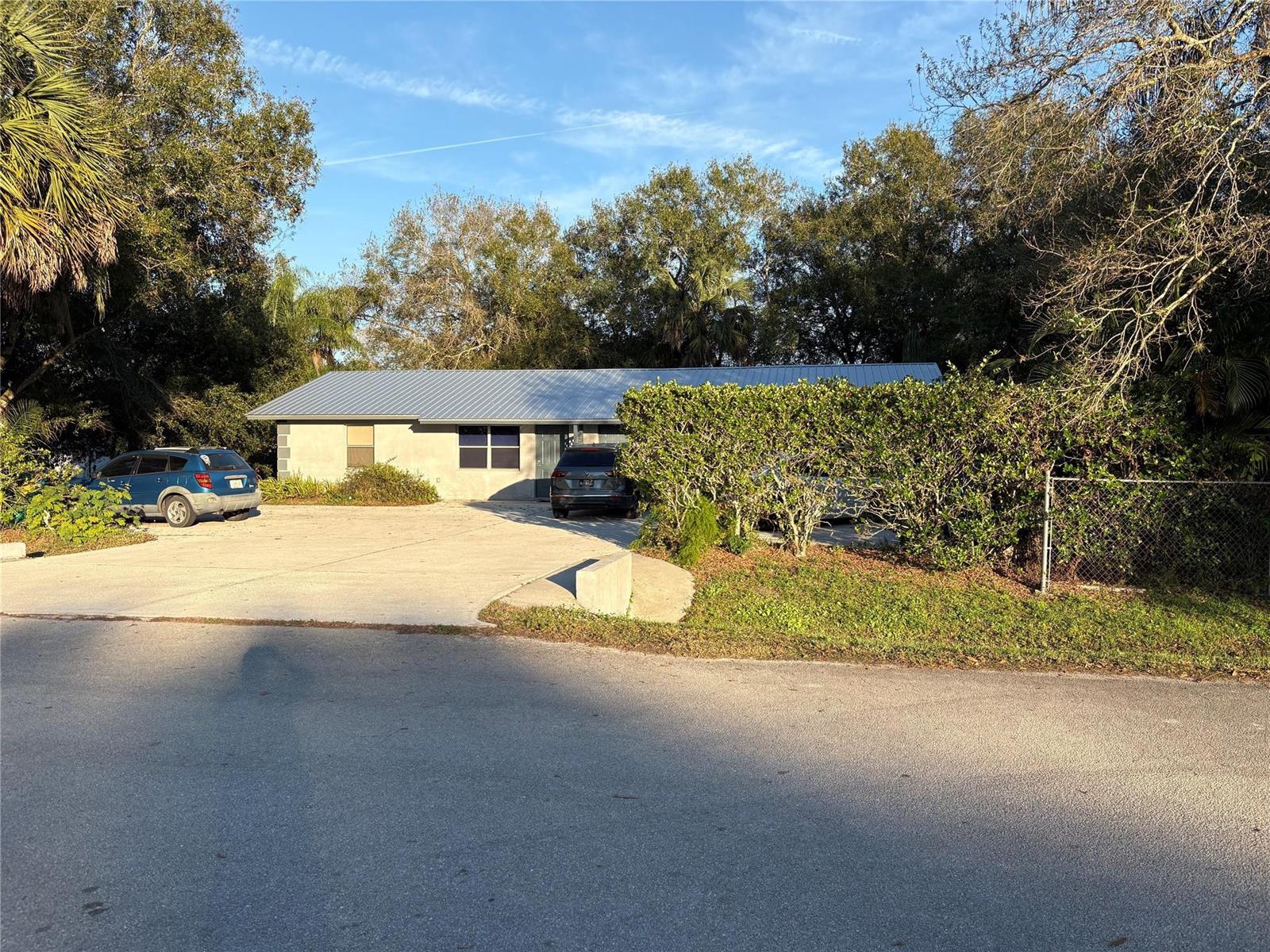 A single-story house with a metal roof and a concrete driveway sits behind large hedges — 540 NW 24th Avenue, Okeechobee FL 34972, OKEECHOBEE, FL