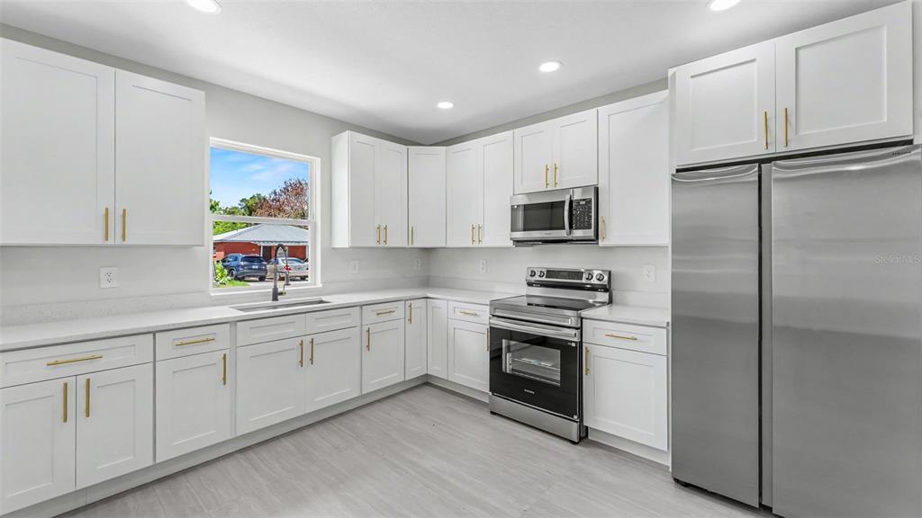 A modern kitchen features white shaker cabinets, stainless steel appliances, and light-colored wood-look flooring — 46 ASH STREET, HAINES CITY, FL