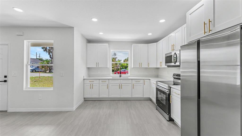 A modern kitchen features white cabinets, stainless steel appliances, and light wood-look flooring — 46 ASH STREET, HAINES CITY, FL