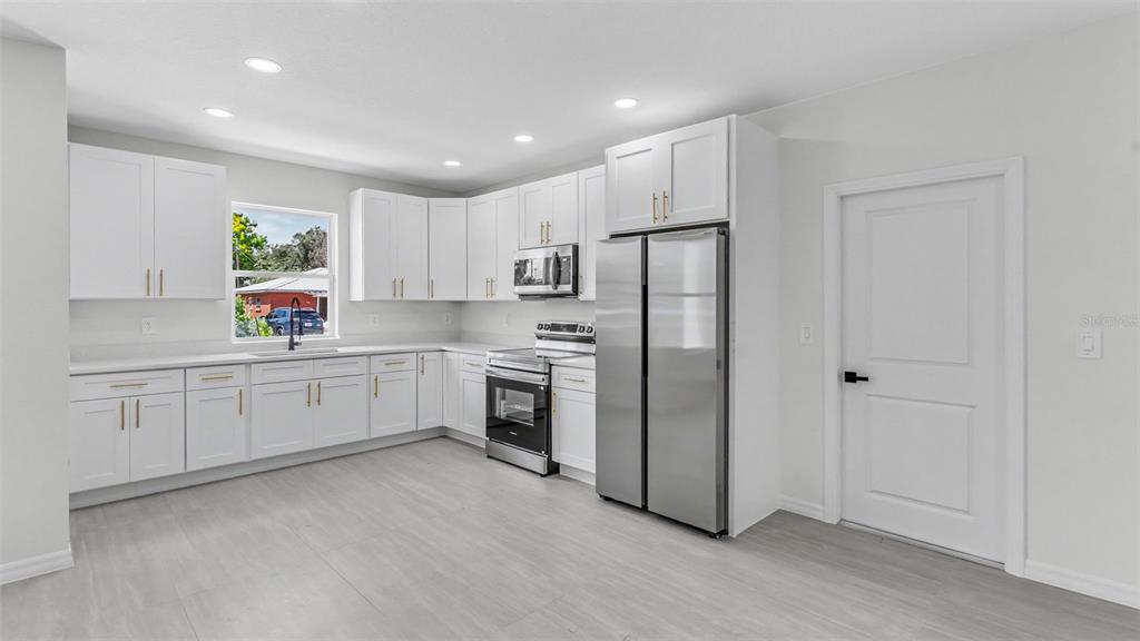 A modern kitchen features white cabinets, stainless steel appliances, and light-colored flooring — 46 ASH STREET, HAINES CITY, FL