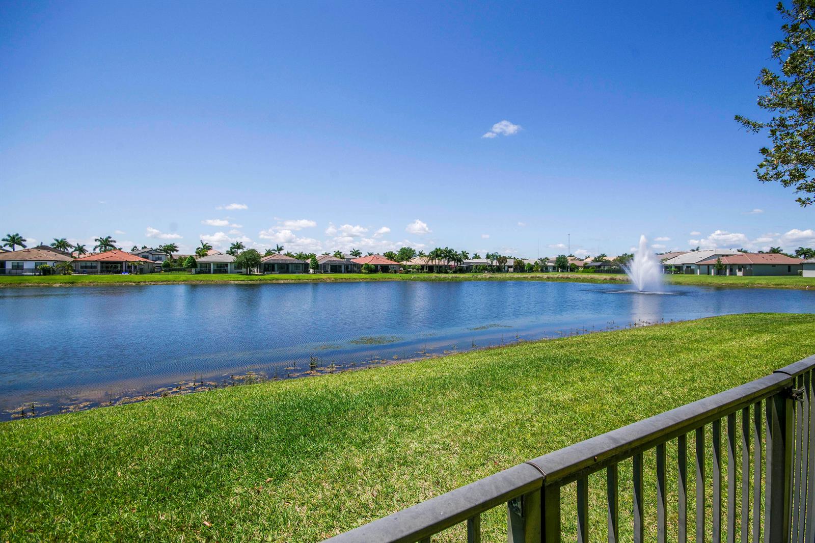 A view of a lake with a fountain, surrounded by houses and a grassy lawn — 8301 Rearing Lane, Lake Worth FL 33467, LAKE WORTH, FL