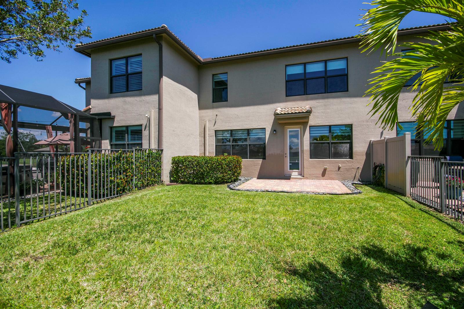 The backyard features a small brick patio, a green lawn, and a metal fence — 8301 Rearing Lane, Lake Worth FL 33467, LAKE WORTH, FL