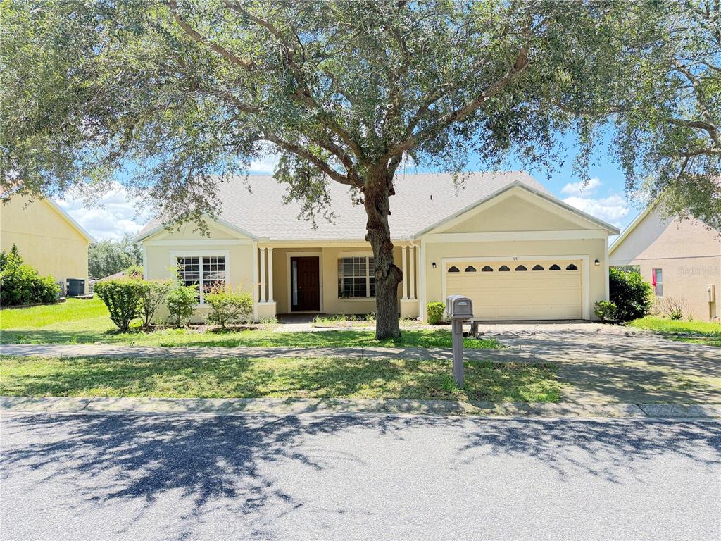 A single-story yellow house with a two-car garage and a large tree in front — 1751 SOUTHERN OAK LOOP, MINNEOLA, FL