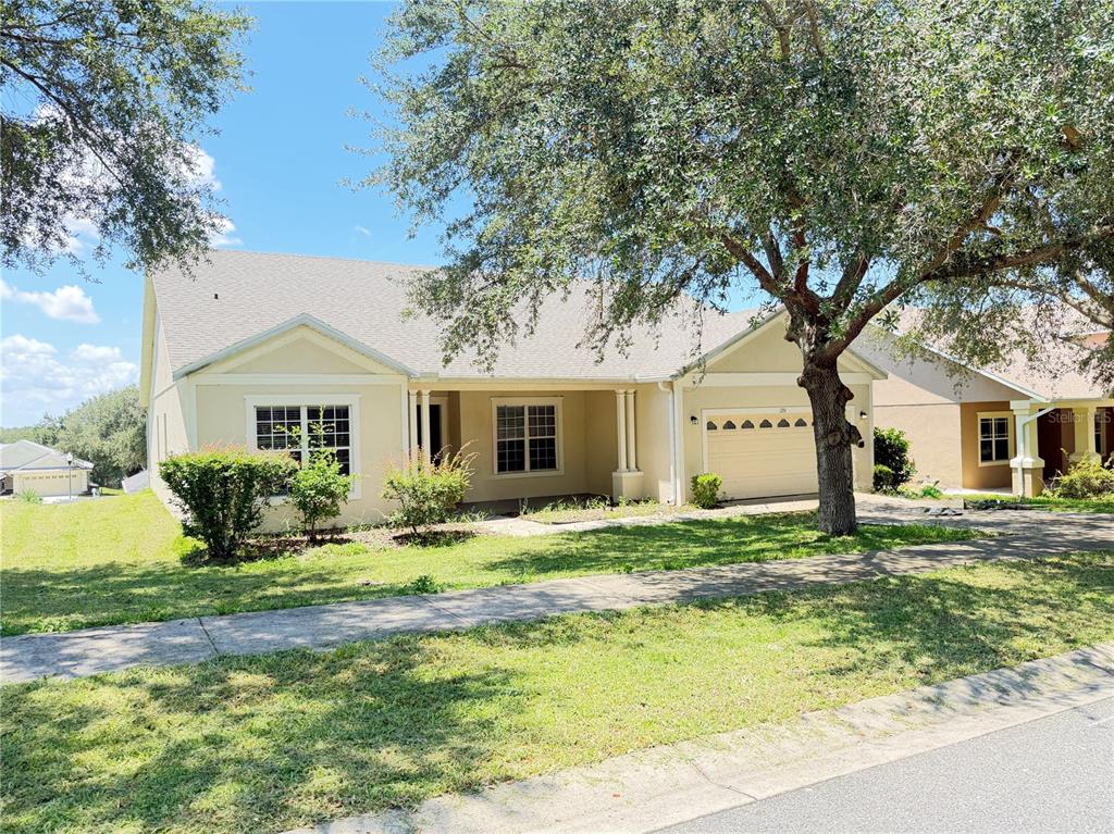 A single-story tan house with a two-car garage and a large tree in the front — 1751 SOUTHERN OAK LOOP, MINNEOLA, FL