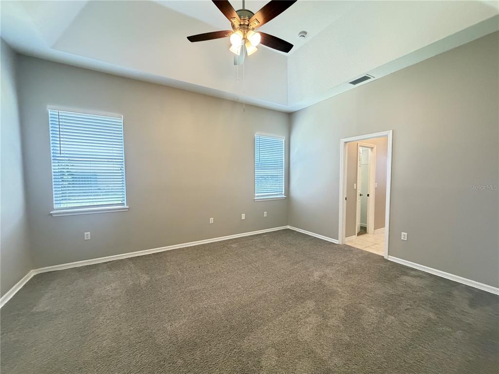 A bedroom with gray carpet, neutral walls, a tray ceiling, and a ceiling fan — 1751 SOUTHERN OAK LOOP, MINNEOLA, FL