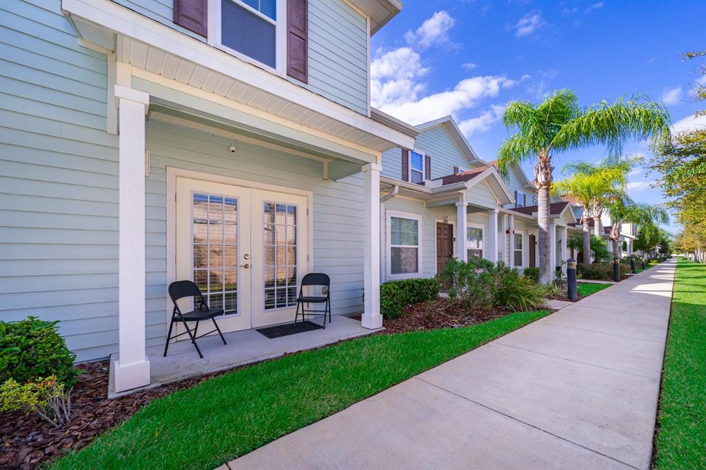 A light blue townhouse exterior features a covered patio with two chairs and a sidewalk — 8913 W SHINE DRIVE, KISSIMMEE, FL