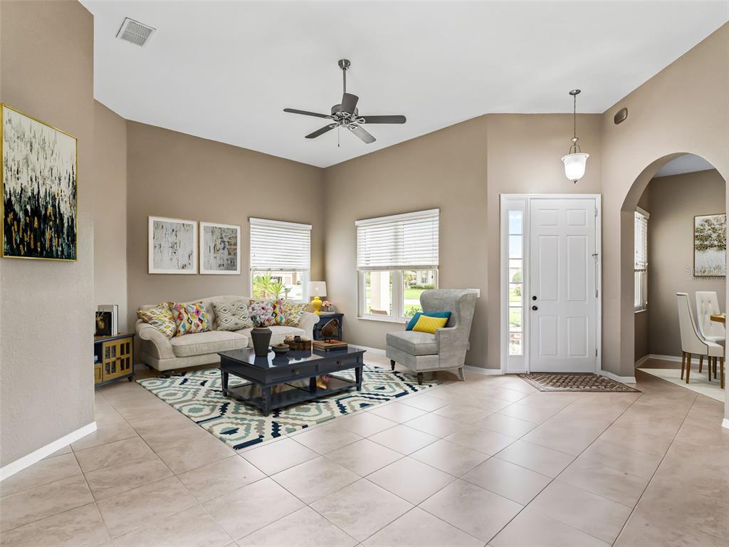 A living room features tile flooring, a ceiling fan, a sofa, and an entryway door — 11972 SE 176TH PLACE ROAD, SUMMERFIELD, FL