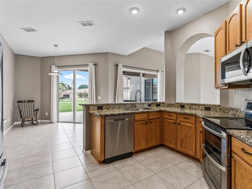 A kitchen with oak cabinets, granite countertops, and stainless steel appliances overlooks a dining area — 11972 SE 176TH PLACE ROAD, SUMMERFIELD, FL