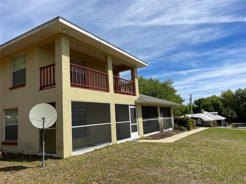 A two-story yellow house features a screened-in porch and an upper-level balcony with red railings — 15121 SE 175TH STREET, WEIRSDALE, FL