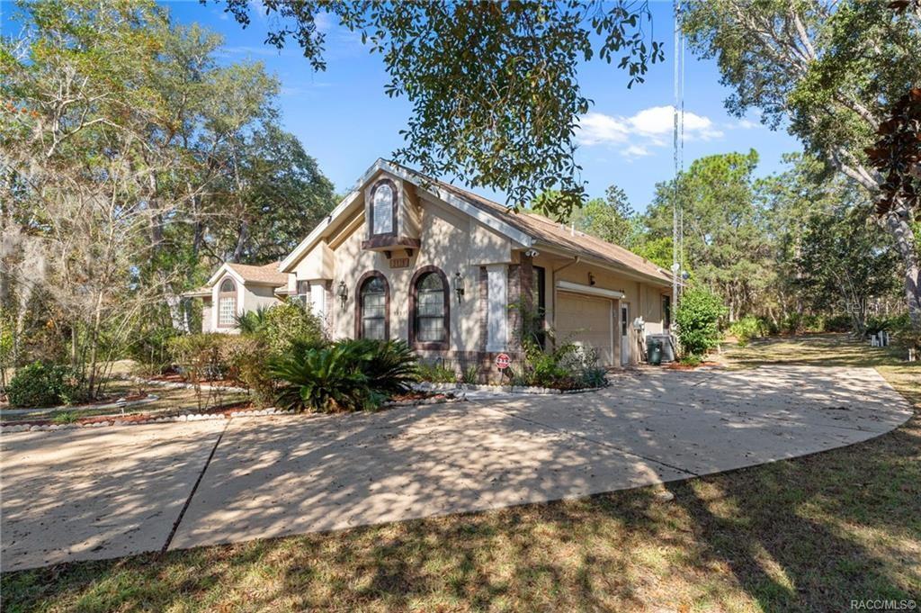 A tan house with a concrete driveway and arched windows sits in a wooded lot — 3135 N BUCKHORN DRIVE, BEVERLY HILLS, FL