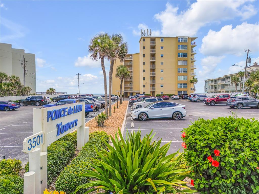 A multi-story tan apartment building stands behind a parking lot with a prominent sign — 3501 S ATLANTIC AVENUE UNIT 2060, NEW SMYRNA BEACH, FL