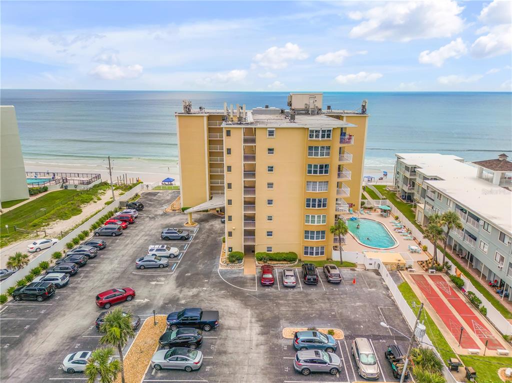 An aerial view shows a multi-story beachfront condominium building with a parking lot and pool — 3501 S ATLANTIC AVENUE UNIT 2060, NEW SMYRNA BEACH, FL