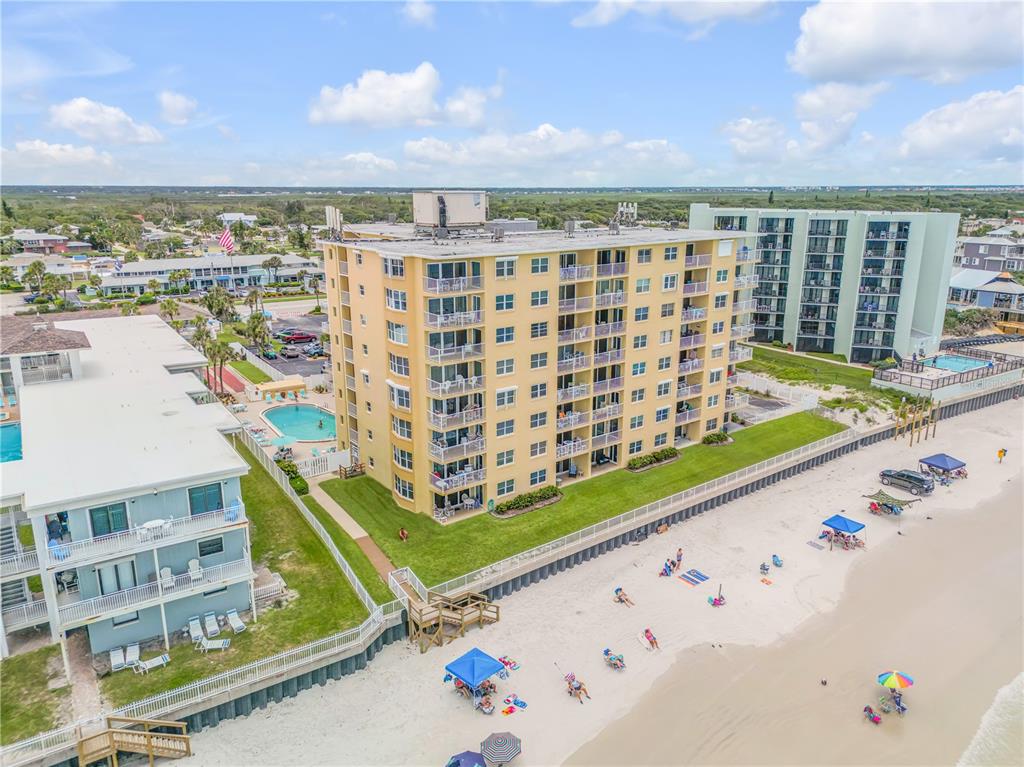 An aerial view shows a multi-story yellow apartment building situated directly on a sandy beach — 3501 S ATLANTIC AVENUE UNIT 2060, NEW SMYRNA BEACH, FL