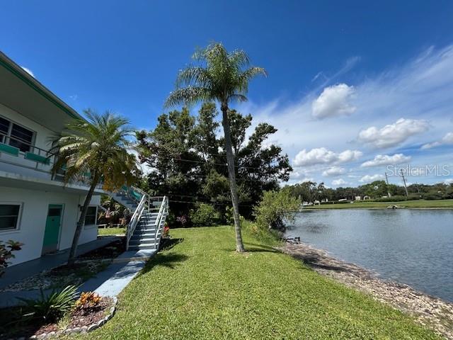 A white multi-story building sits beside a grassy lawn and a lake with palm trees — 6100 21ST STREET N UNIT 15, ST PETERSBURG, FL