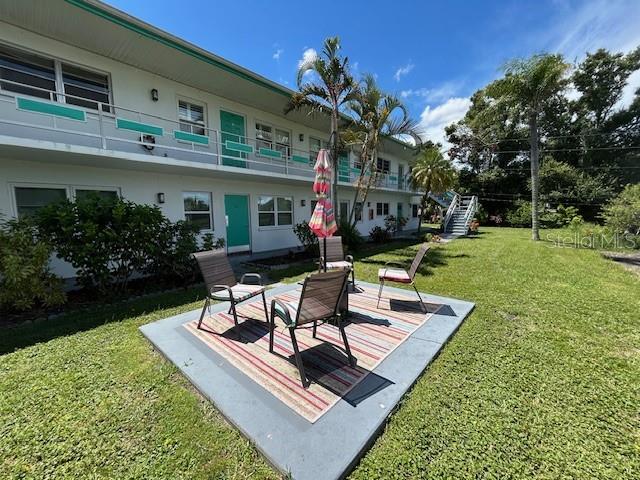 A patio with chairs and an umbrella sits on a lawn outside a multi-story building — 6100 21ST STREET N UNIT 15, ST PETERSBURG, FL