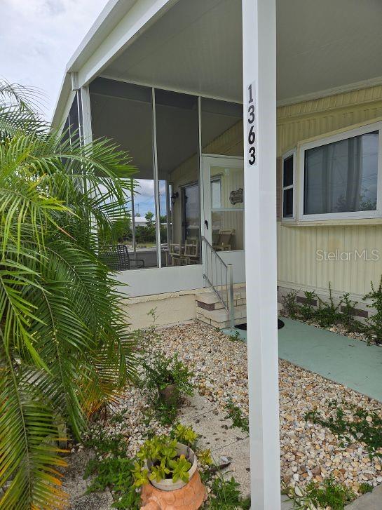 A mobile home exterior features a screened-in porch, a white support post, and gravel landscaping — 1363 SEAGULL DRIVE, ENGLEWOOD, FL
