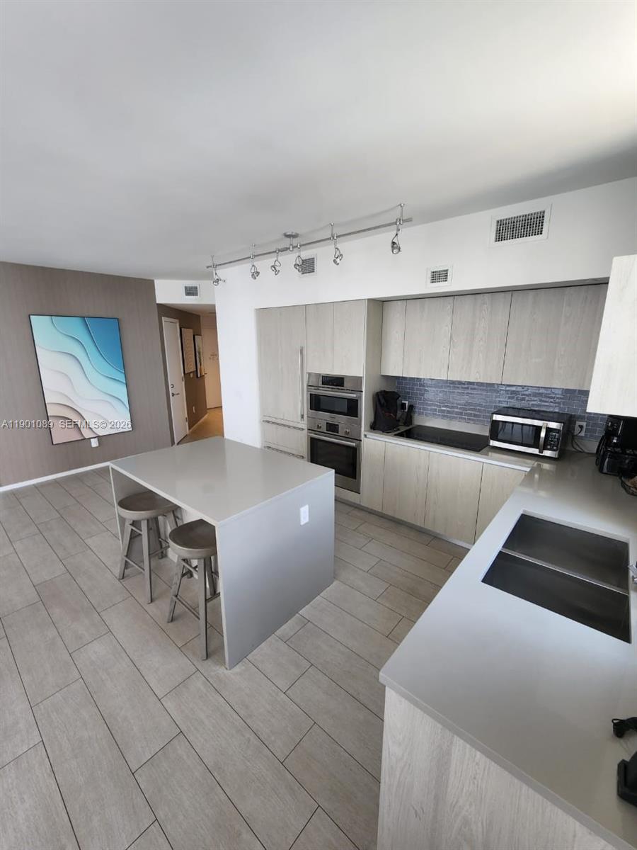 A modern kitchen features light wood cabinetry, a central island with stools, and tile flooring — 4010 S Ocean Dr # R1709, Hollywood FL 33019, HOLLYWOOD, FL