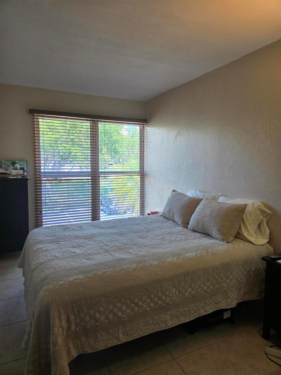 A bedroom features a bed with a textured quilt, two pillows, and a window with blinds — 8324 SW 103rd Avenue, Miami FL 33173, MIAMI, FL