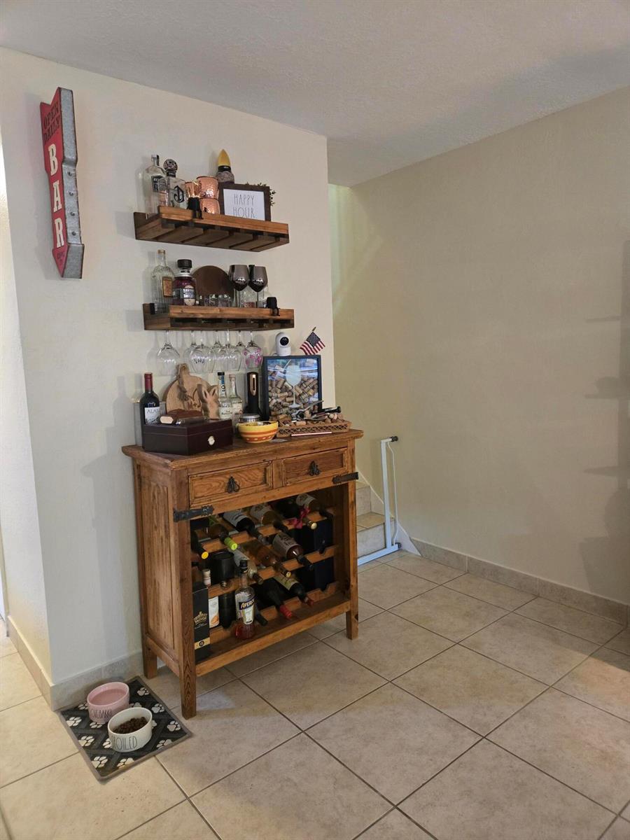 A wooden bar cabinet with wine storage and wall-mounted shelves sits on a tiled floor — 8324 SW 103rd Avenue, Miami FL 33173, MIAMI, FL