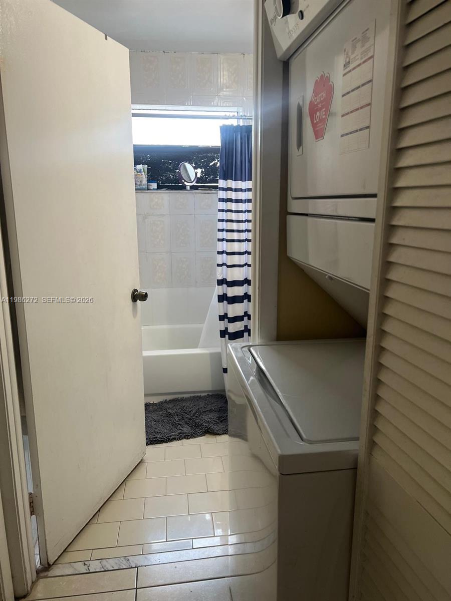 A laundry area with a stacked washer and dryer sits beside a bathroom with tile — 2295 W 53rd Pl # 201, Hialeah FL 33016, HIALEAH, FL