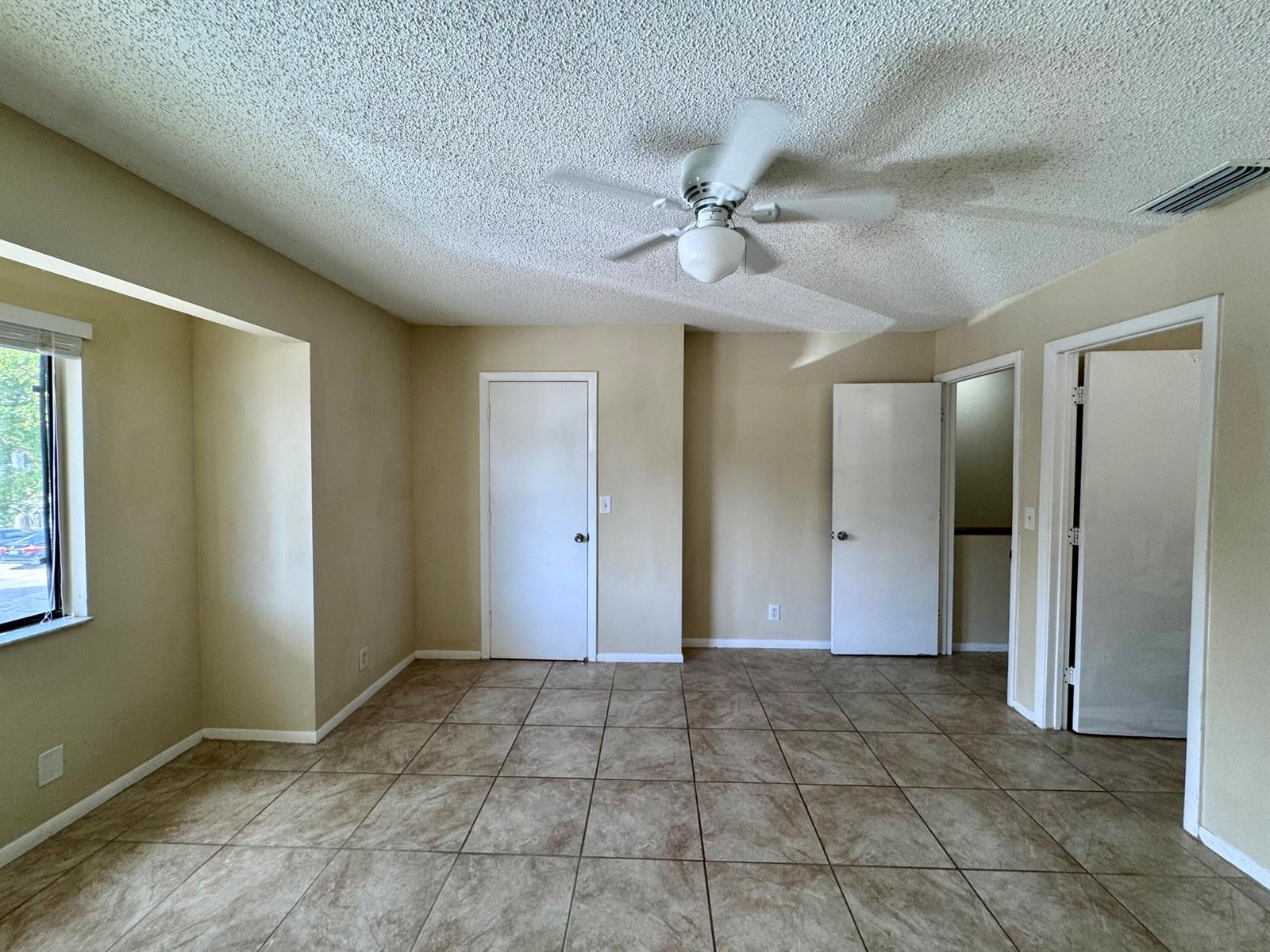 An empty room with beige walls, tile flooring, a ceiling fan, and three white doors — 704 Riverside Drive, FL 33463, FL