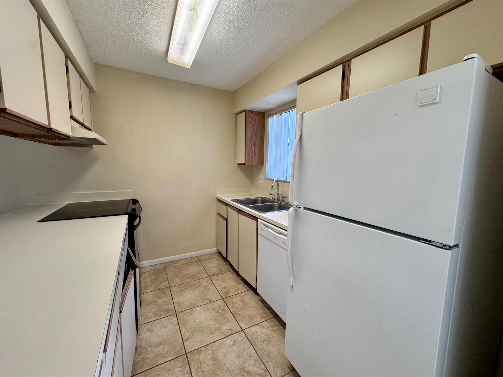 A kitchen features white appliances, beige cabinets, tile flooring, and a double-basin sink — 704 Riverside Drive, FL 33463, FL