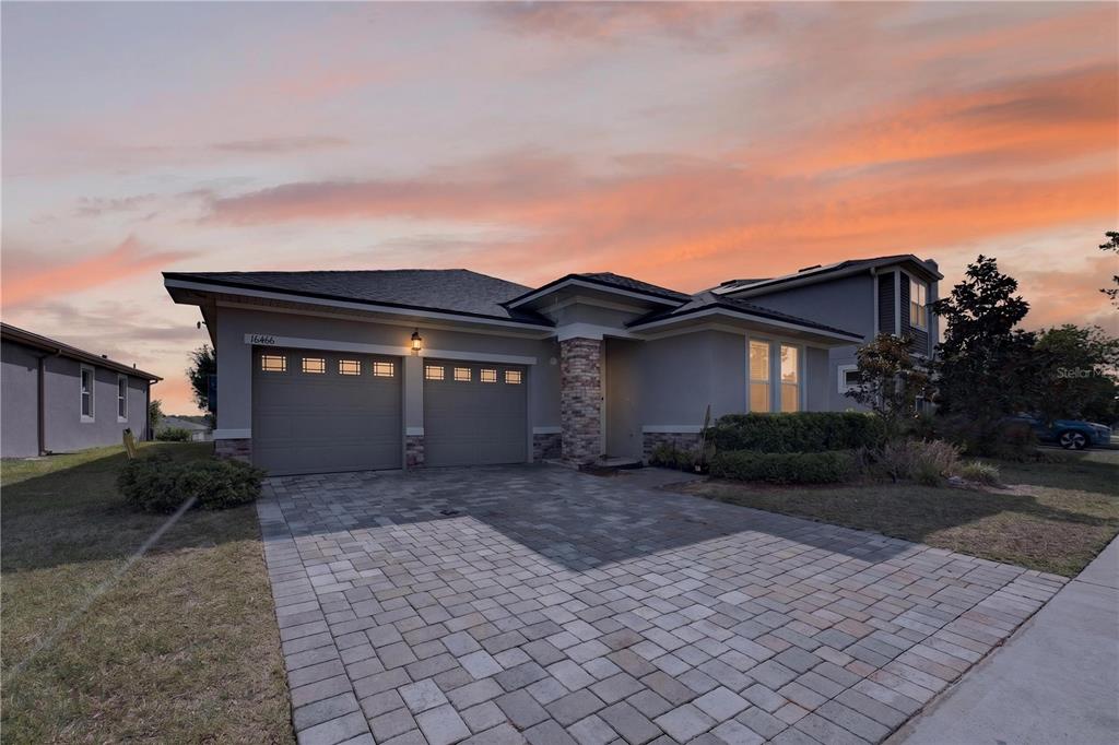 A single-story house with a two-car garage and a stone-accented entryway at sunset — 16466 OLIVE HILL DRIVE, WINTER GARDEN, FL