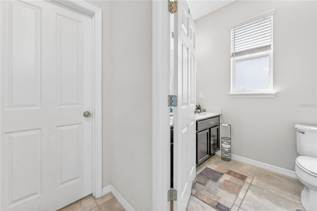 A bathroom with a dark vanity, a toilet, a window with blinds, and tiled flooring — 16466 OLIVE HILL DRIVE, WINTER GARDEN, FL