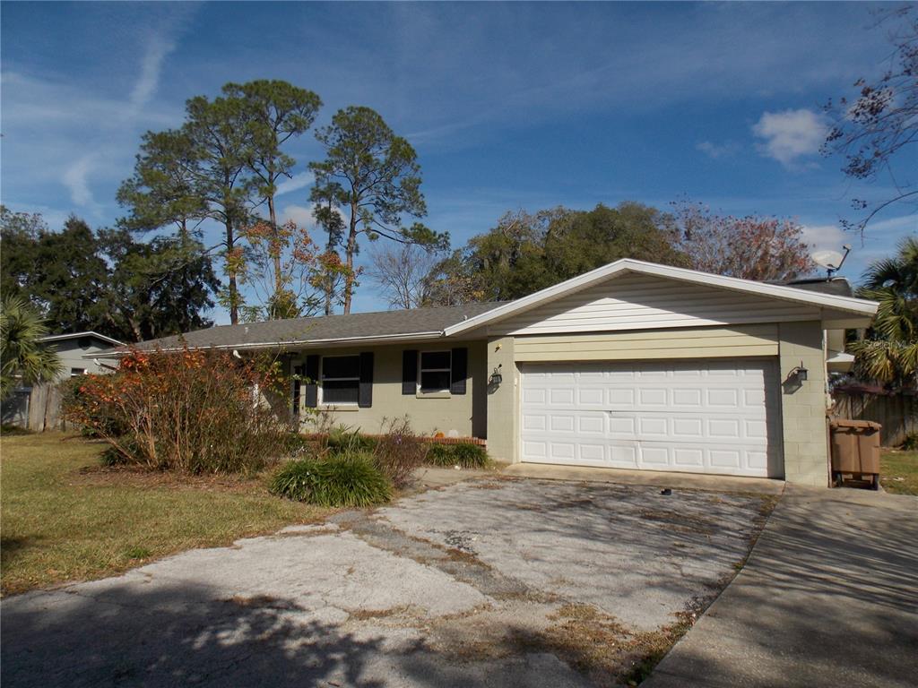 A single-story house with a white garage door, light-colored siding, and a cracked concrete driveway — 1827 SE 7TH AVENUE, OCALA, FL