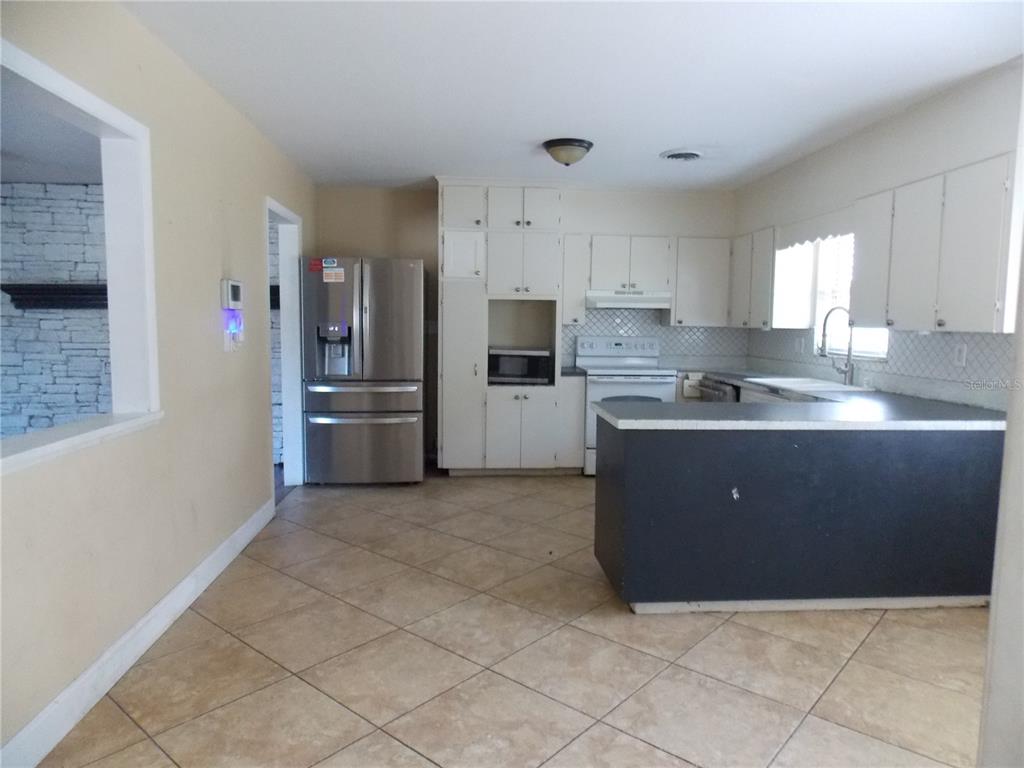 A kitchen features white cabinetry, stainless steel appliances, a dark island, and beige tile flooring — 1827 SE 7TH AVENUE, OCALA, FL