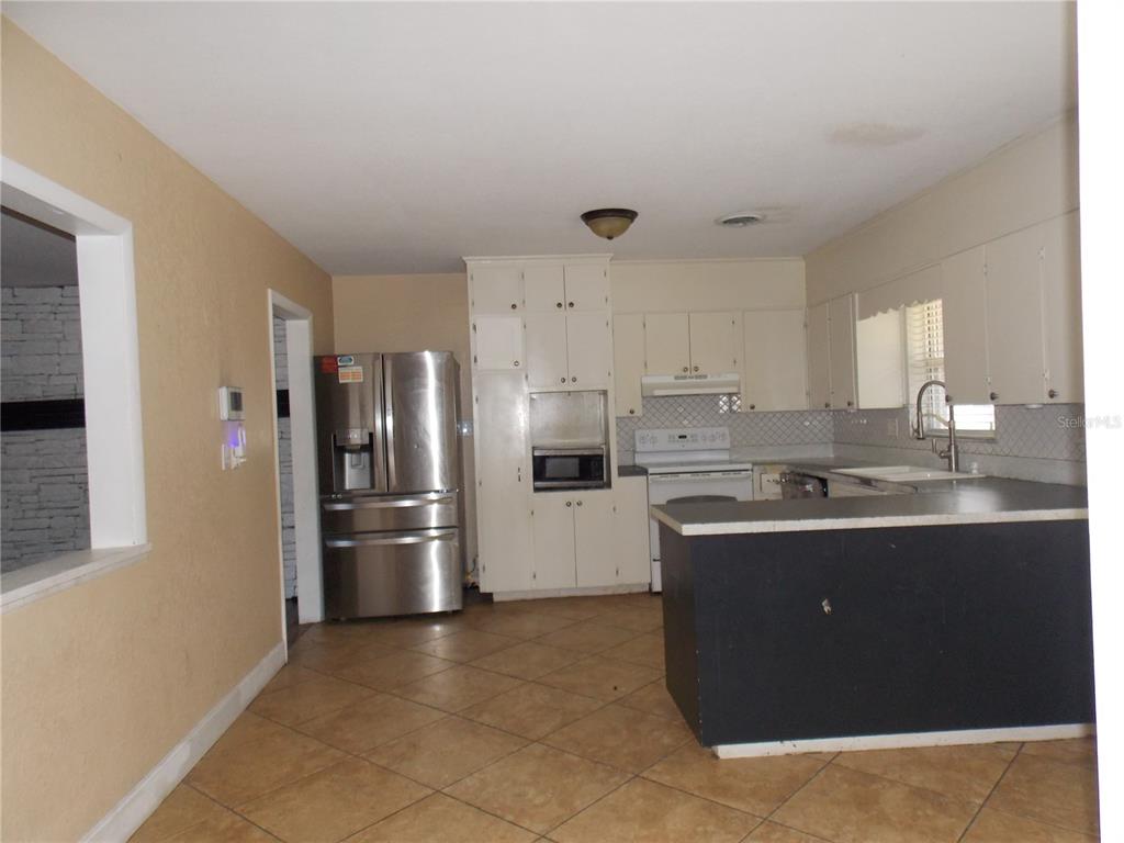 A kitchen features tan walls, tile flooring, white cabinets, stainless steel appliances, and a peninsula — 1827 SE 7TH AVENUE, OCALA, FL