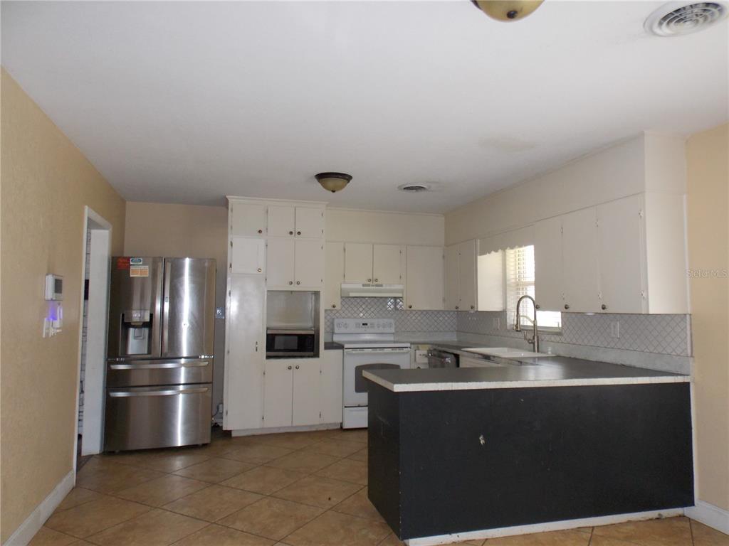 A kitchen features white cabinetry, stainless steel appliances, a black peninsula, and tiled flooring — 1827 SE 7TH AVENUE, OCALA, FL