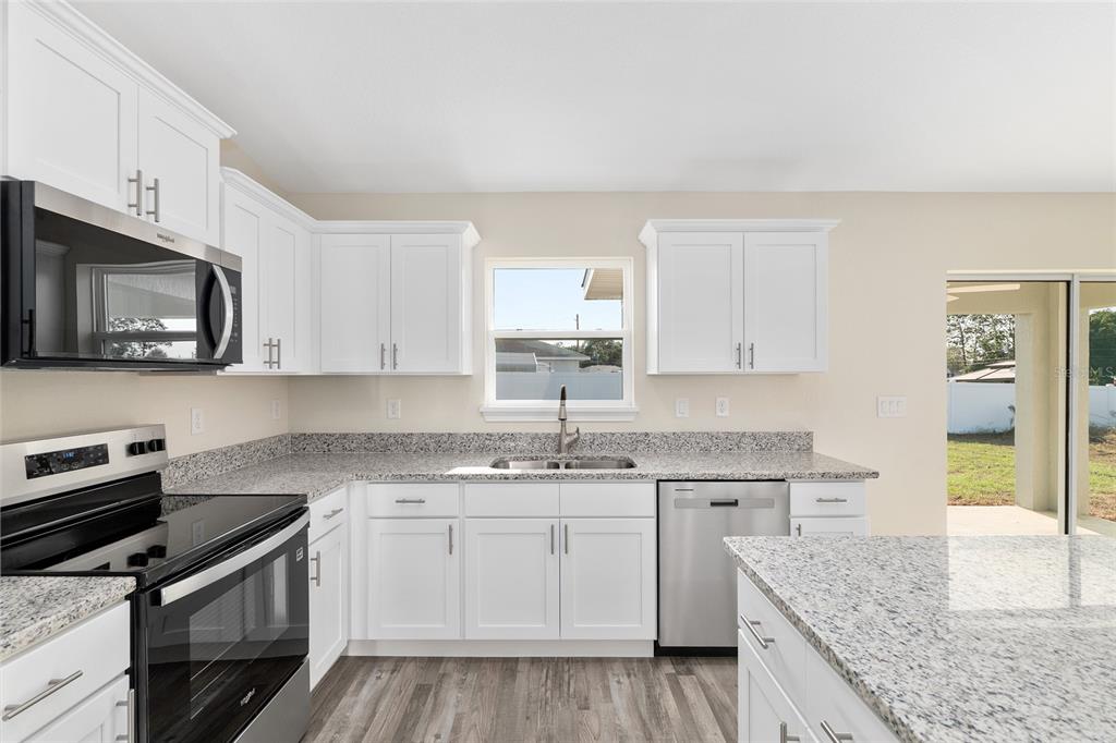 A kitchen with white cabinets, granite countertops, stainless steel appliances, and wood-look flooring — 93 PECAN PASS, OCALA, FL