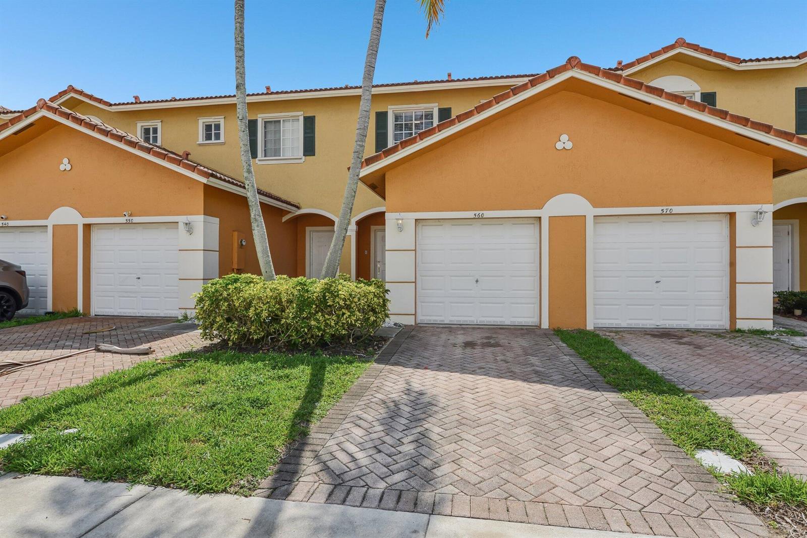 An exterior view of a multi-unit townhouse complex with orange stucco walls and garage doors — 560 St Tropez Lane, Margate FL 33068, MARGATE, FL