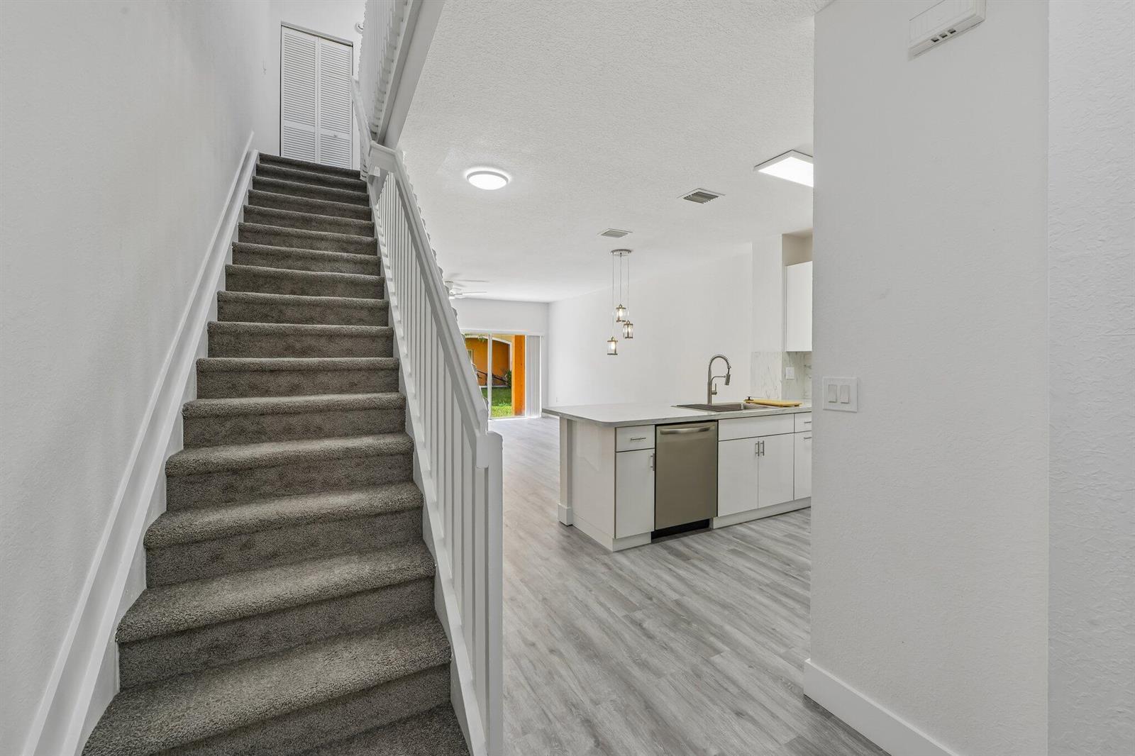A carpeted staircase leads to an open-concept kitchen with white cabinets and light flooring — 560 St Tropez Lane, Margate FL 33068, MARGATE, FL