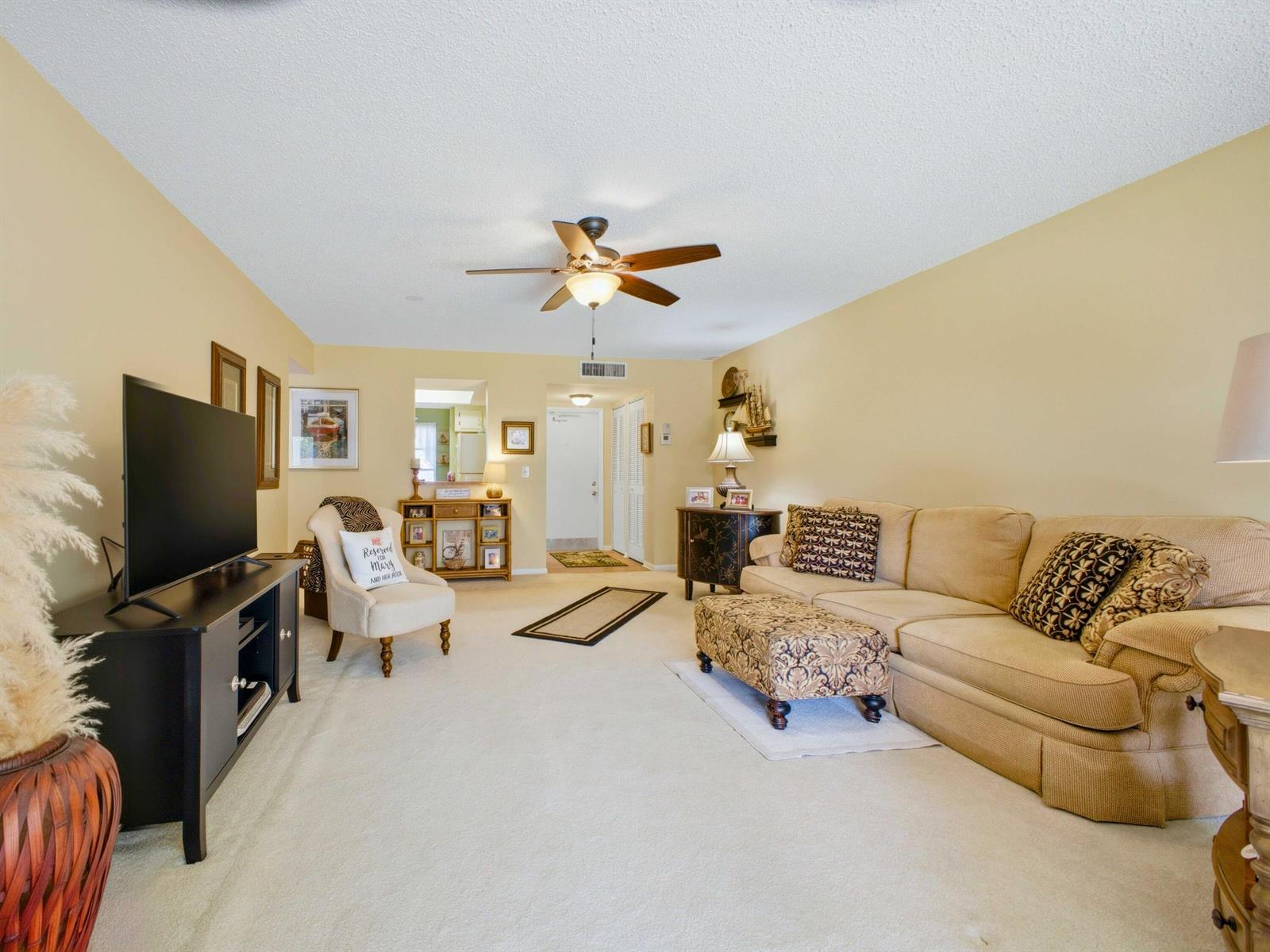 A living room features beige walls, a tan sofa, a television, and a ceiling fan — 6625 S Oriole Boulevard # 2040, Delray Beach FL 33446, DELRAY BEACH, FL